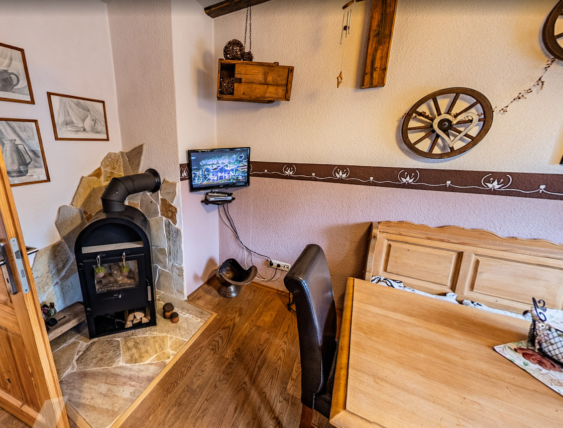 Kleiner Aufenthaltsraum der Pension Kluge in Freiberg mit Holzofen, Fernseher und gemütlicher Sitzecke.